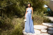 Woman in a blue dress standing on a stone path with greenery around
