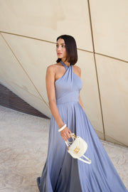 Woman in a long light blue dress holding a white handbag against a modern architectural background
