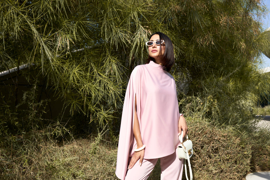 Woman in a pink outfit standing outdoors with greenery in the background