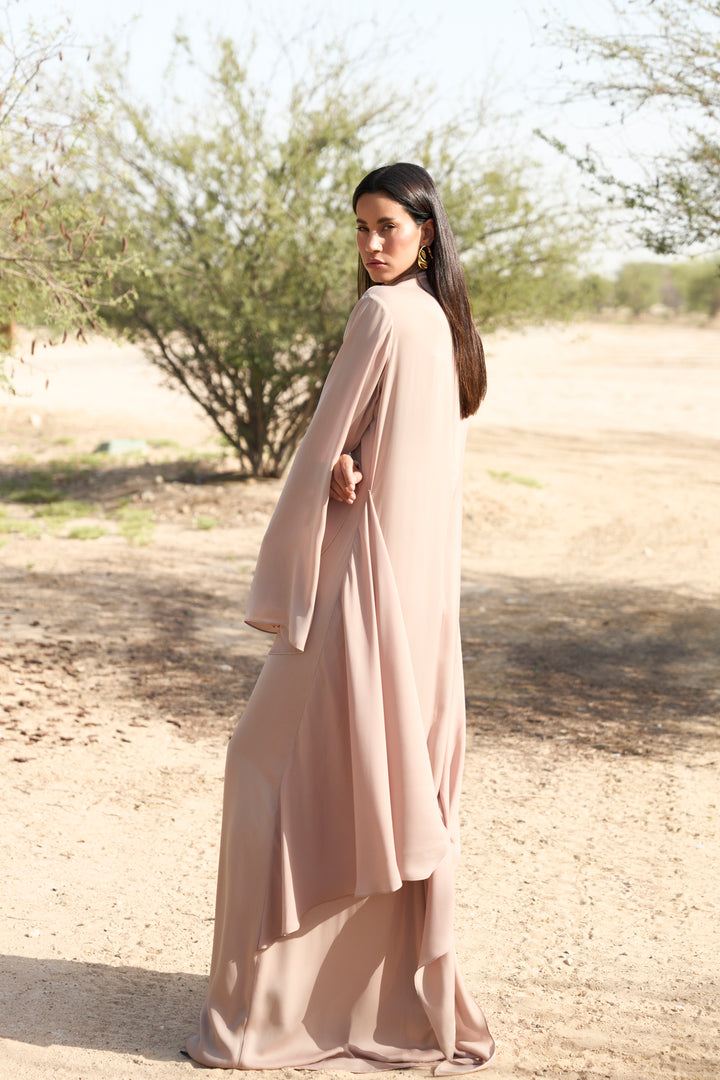 Woman in a long, light-colored dress standing in a desert landscape.