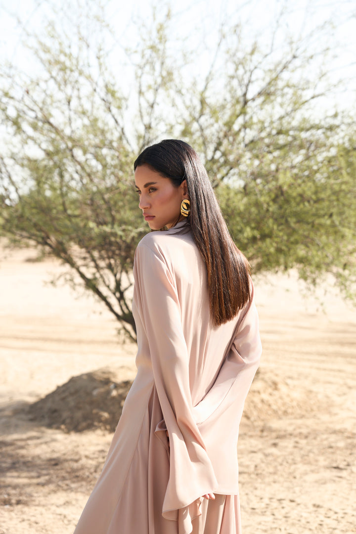 Woman in a beige dress standing in a desert-like setting with trees in the background