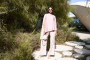Woman in a pink outfit standing outdoors near greenery and a modern building.