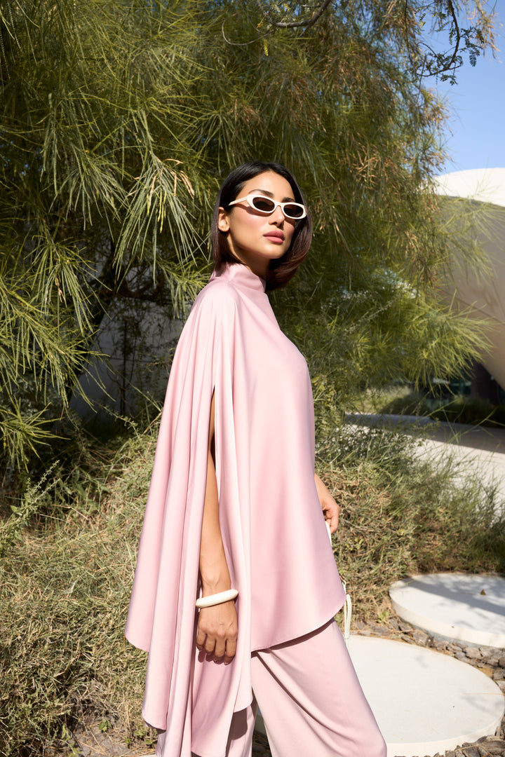 Woman in a pink outfit standing outdoors with greenery in the background