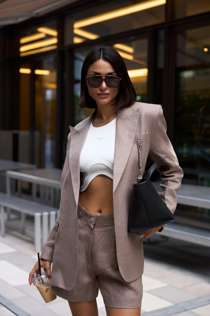 Woman in a beige suit and sunglasses standing outdoors.