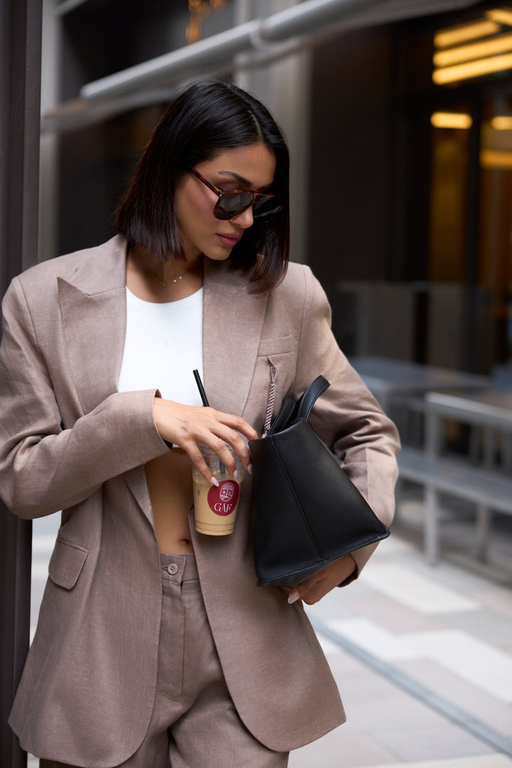 Woman in a beige suit holding a black handbag and a drink with a straw.
