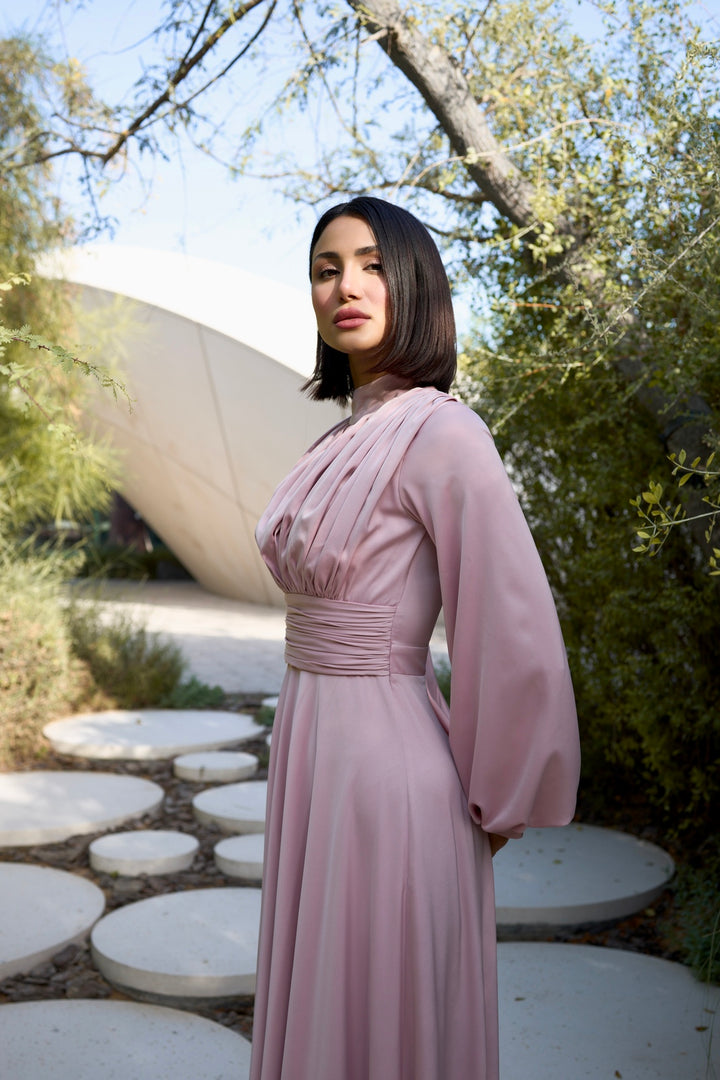 Woman in a pink dress standing outdoors with trees and a sculpture in the background