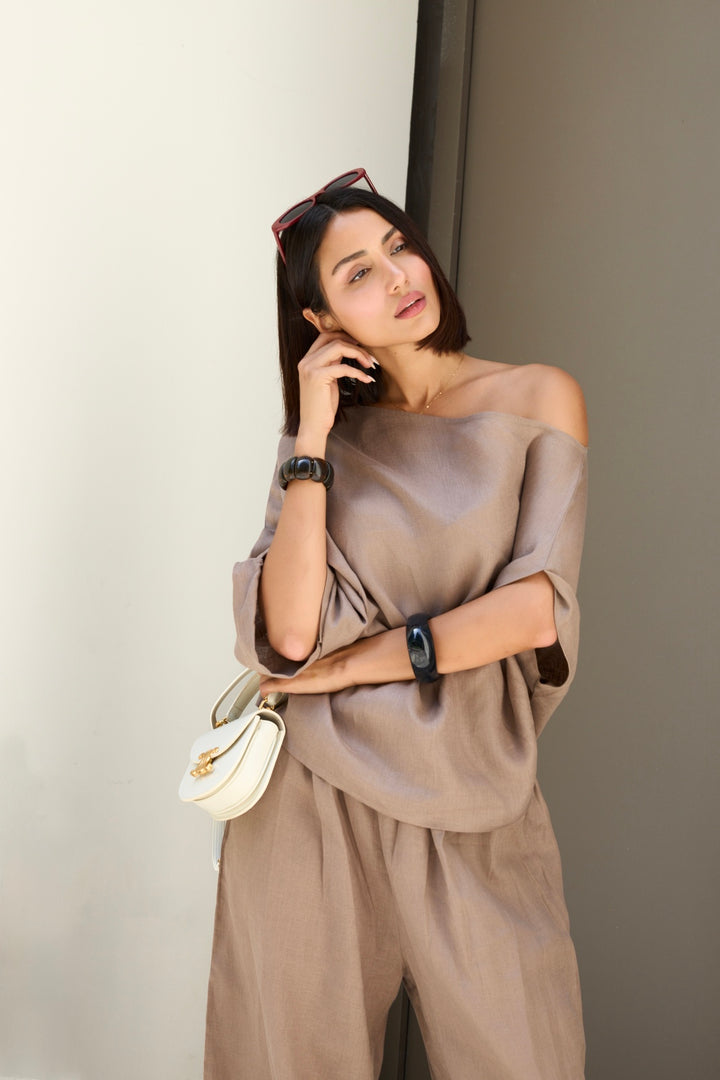 Woman in a beige outfit holding a handbag against a neutral background