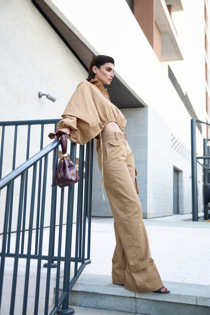 Woman in beige outfit standing on a staircase with a building in the background
