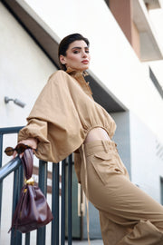 Woman in beige outfit standing outdoors with a handbag.