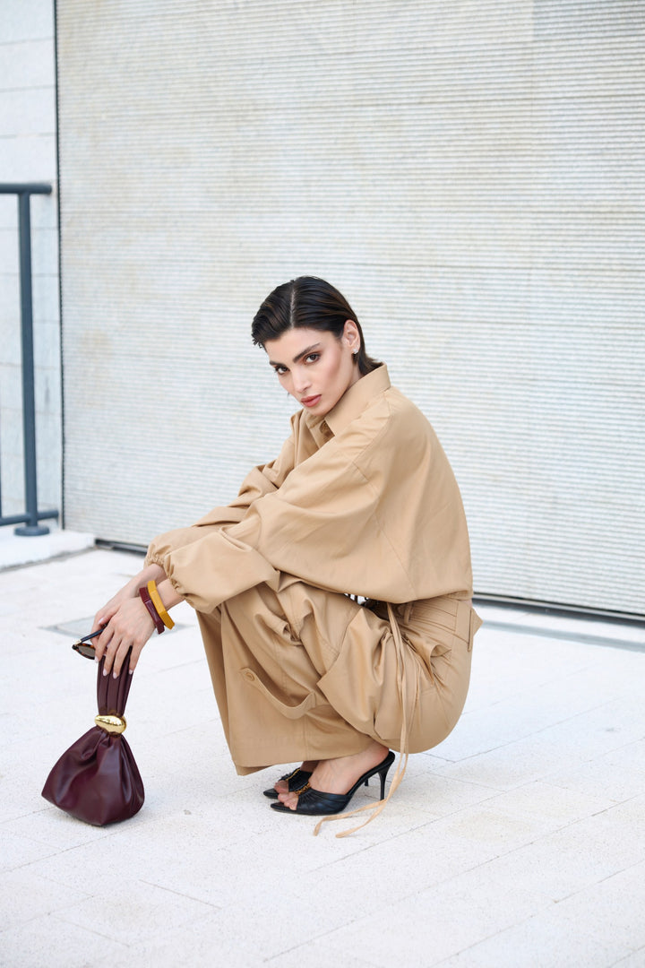 Woman in a beige outfit holding a red handbag against a light-colored wall.