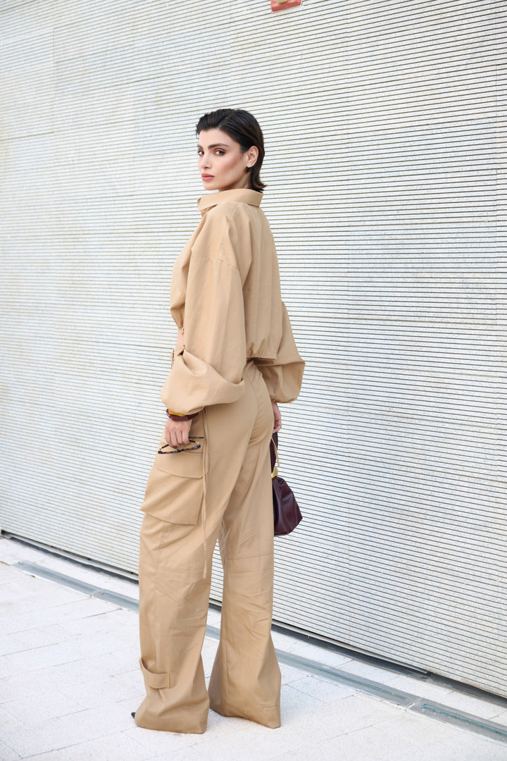 Woman in a beige outfit standing against a light-colored wall.