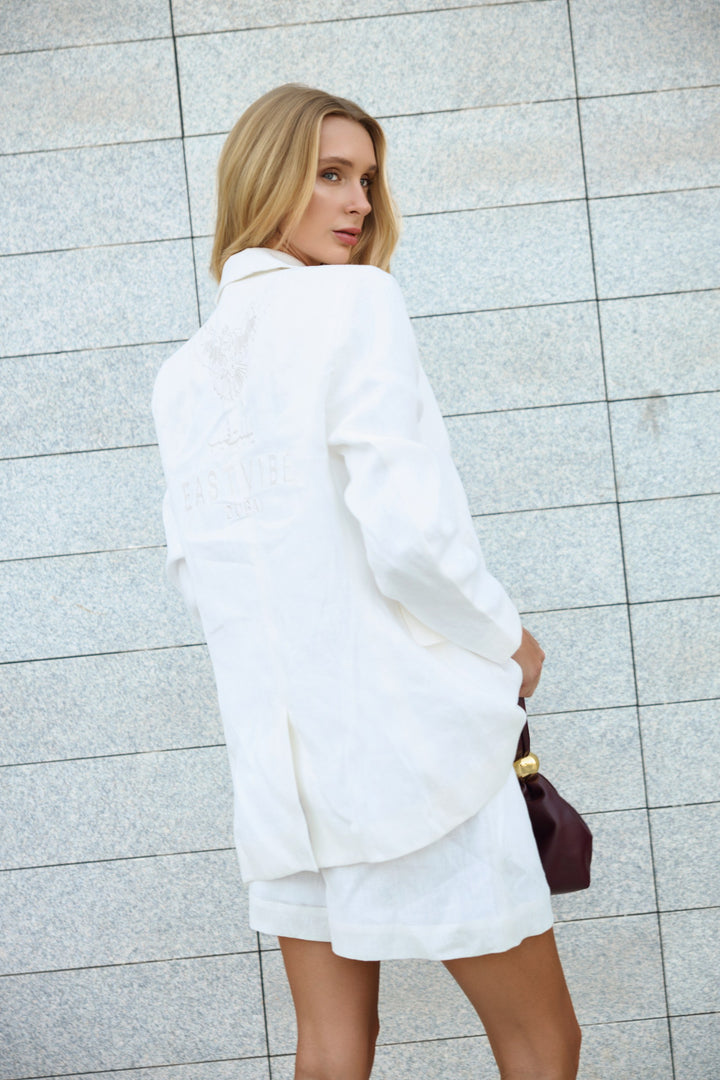 Woman wearing a white outfit against a light gray tiled wall.