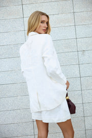 Woman wearing a white outfit against a light gray tiled wall.