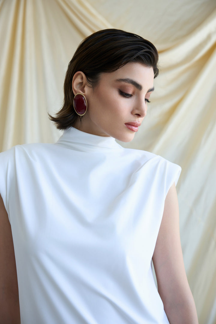 Woman wearing a white sleeveless top against a beige curtain background