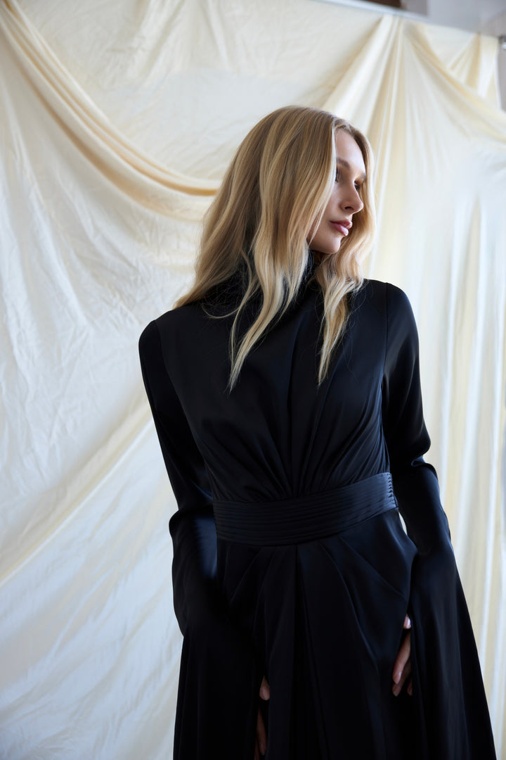 Woman wearing a black dress against a white draped curtain background