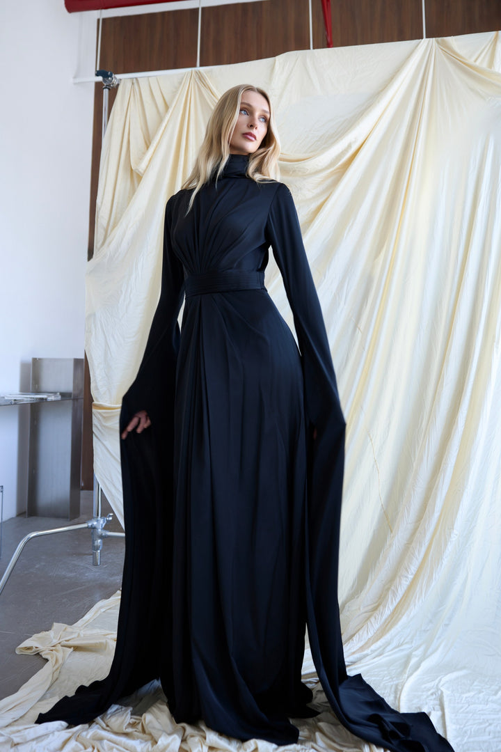 Woman wearing a long black dress standing against a white backdrop