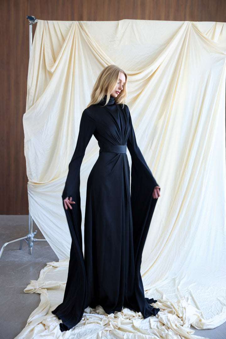 Woman in a black dress standing against a draped white curtain.