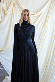 Woman wearing a long black dress with a high collar against a draped white curtain background