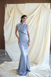 Woman in a light blue evening gown standing against a draped white fabric backdrop.