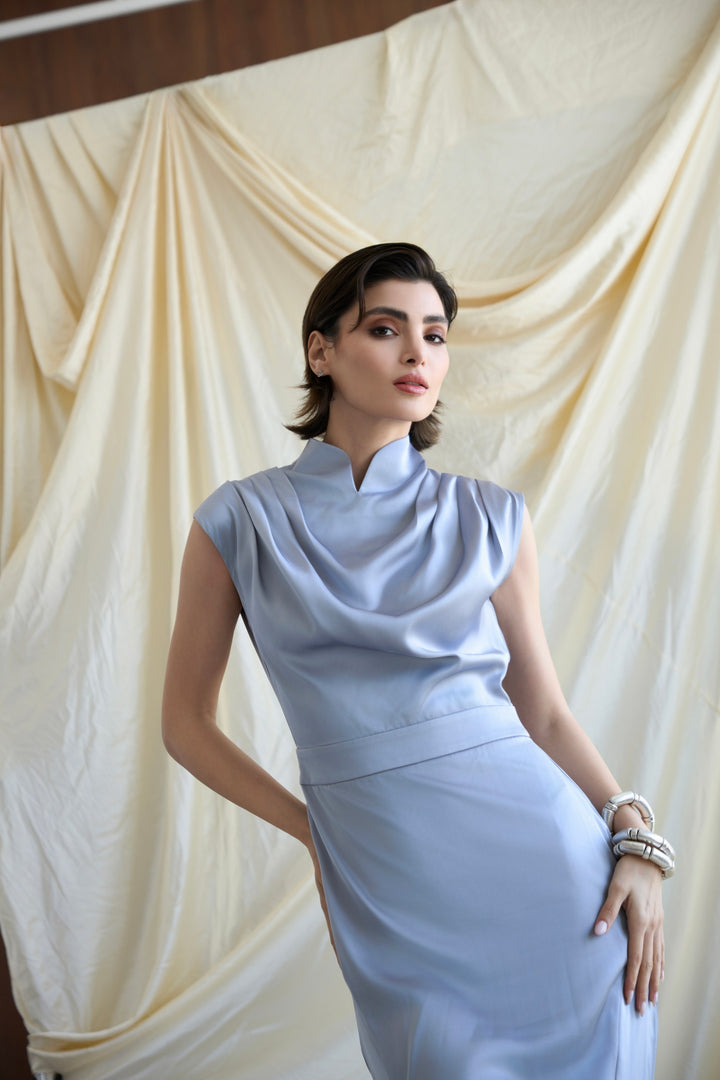 Woman in a light blue dress standing against a beige curtain