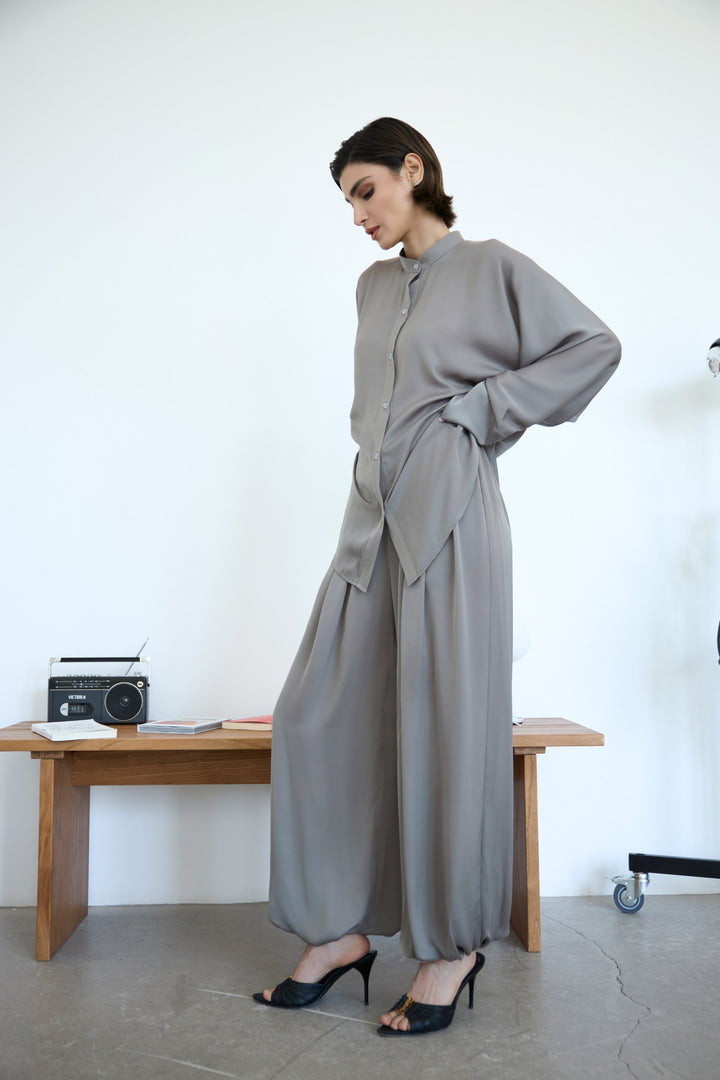 Woman in a gray outfit standing next to a wooden table with a radio on it.