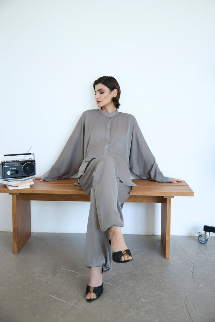Woman in a gray outfit sitting on a wooden bench with a white background