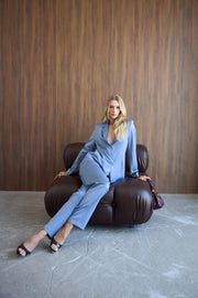 Woman in a blue suit sitting on a brown leather chair against a wooden wall.