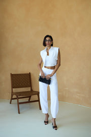 Woman in white outfit standing in a minimalistic room with a chair and beige wall.