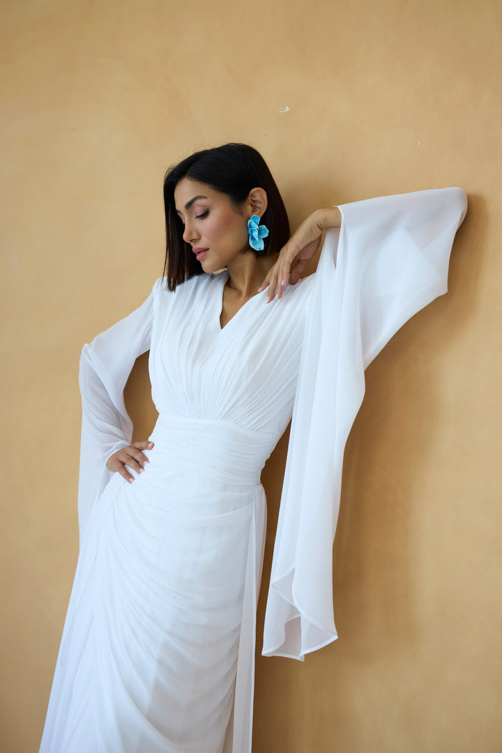 Woman in a white dress with sheer sleeves against a beige wall