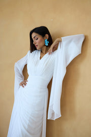 Woman in a white dress with sheer sleeves against a beige wall