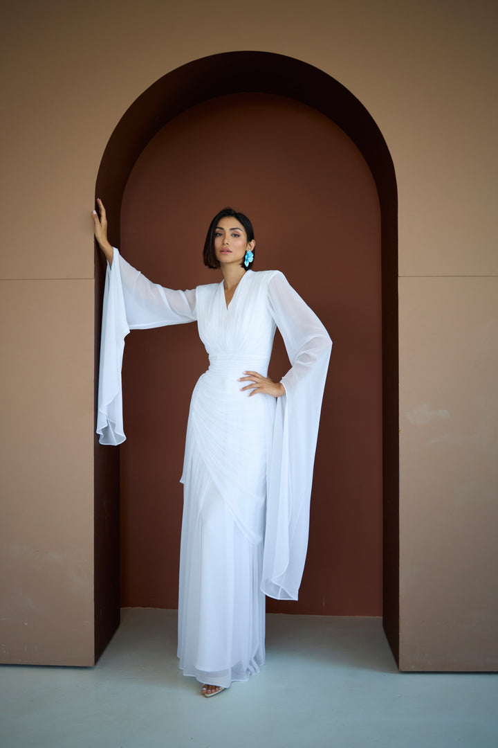 Woman in a white dress standing in an archway with a brown background