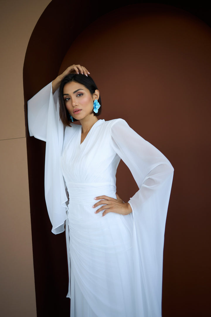 Woman in a white dress with sheer sleeves against a brown background