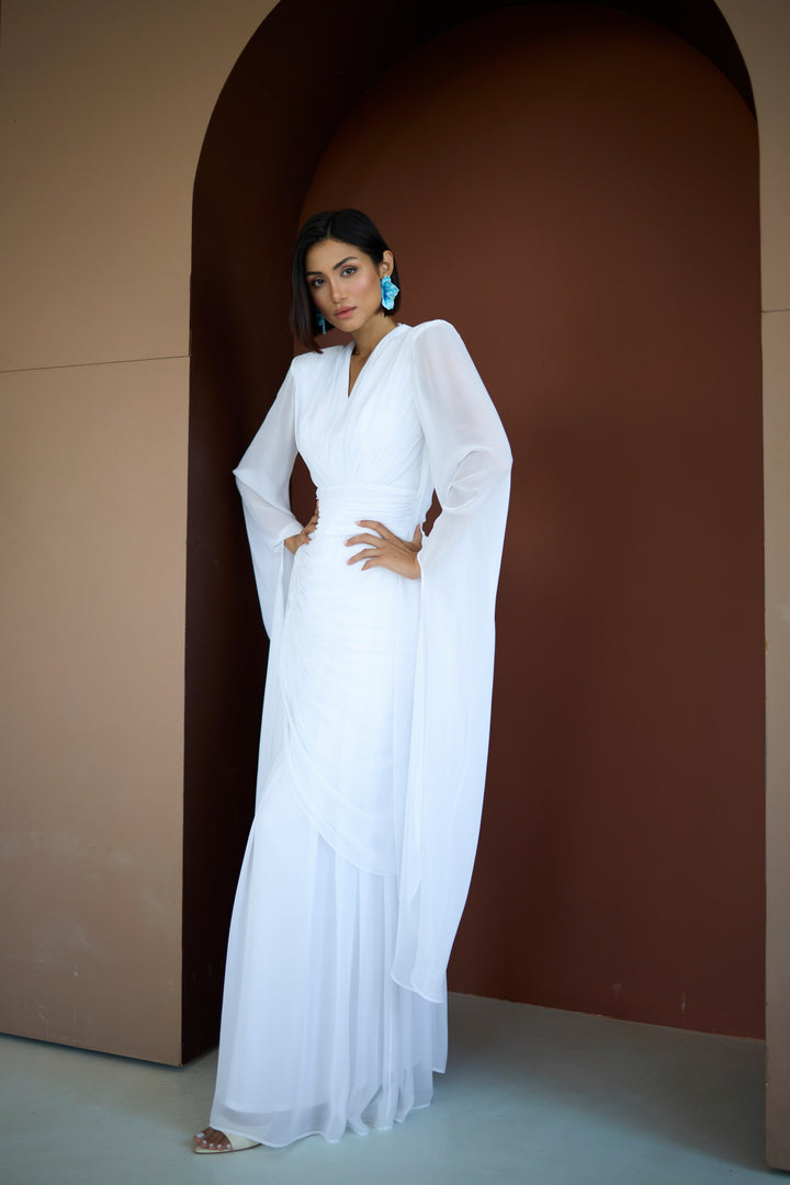 Woman in a white dress standing in a minimalistic setting with a brown archway.