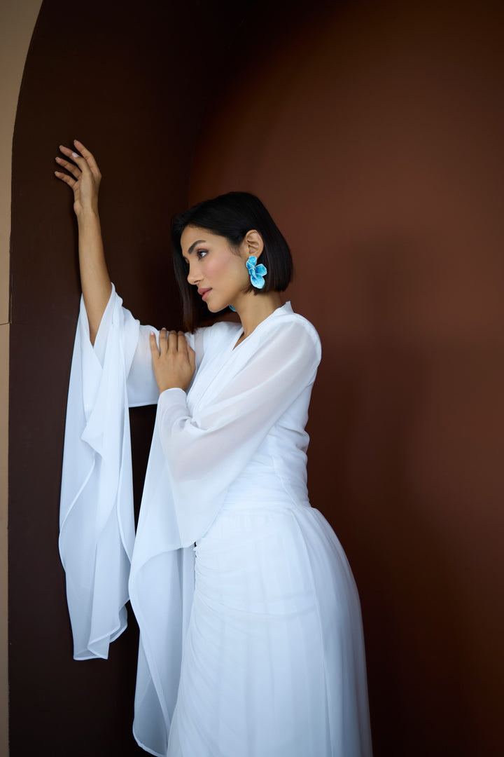 Woman in a white outfit with blue earrings against a brown background
