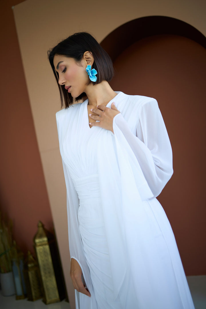 Woman wearing a white saree with blue earrings against a warm-toned background