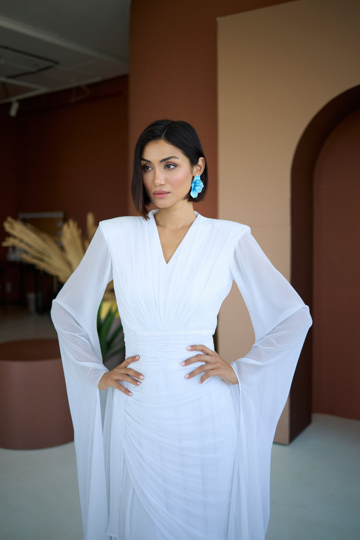 Woman in a white dress standing indoors with a neutral background
