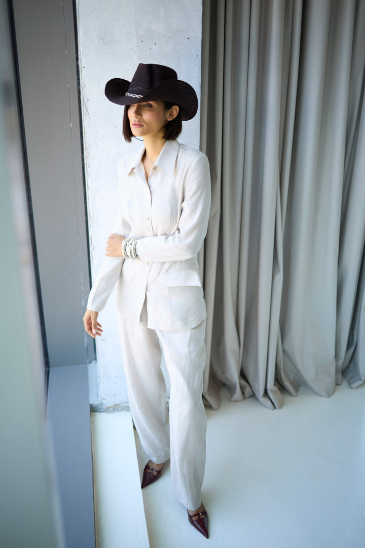 Person wearing a white outfit and black cowboy hat standing against a neutral background