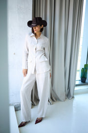 Person wearing a white outfit and black hat in a room with gray curtains and a plant.