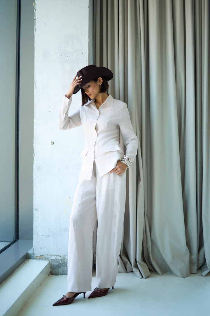 Person wearing a white outfit with a black hat in front of a curtain