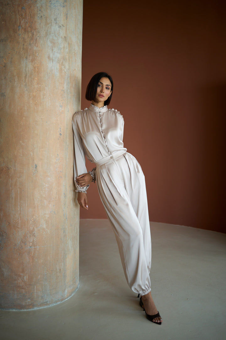Woman in a white outfit standing against a textured wall.