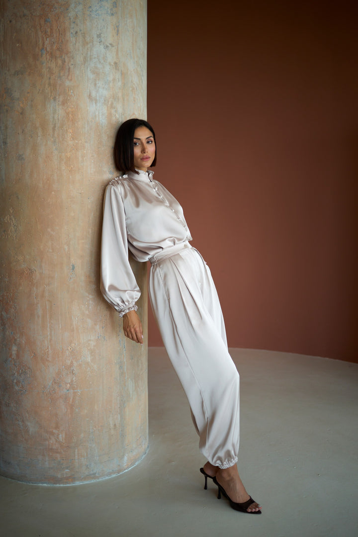 Woman in a white outfit standing against a textured wall and brown background