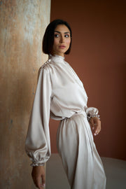Woman in a white outfit standing against a textured wall.