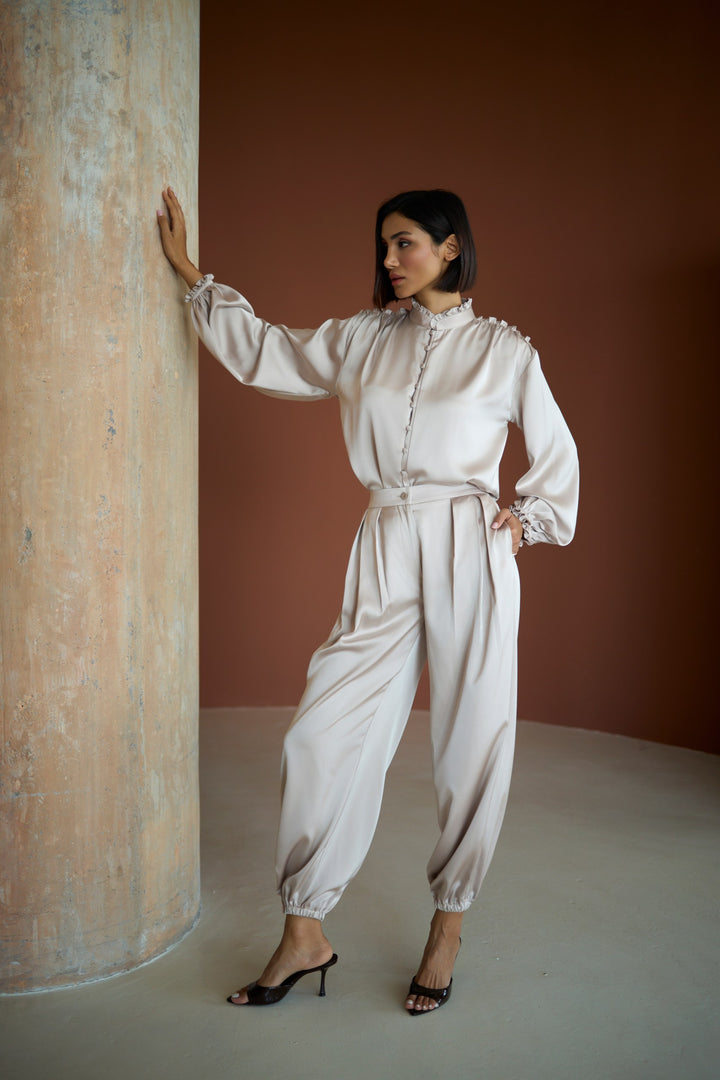 Woman in a white outfit standing against a textured wall.