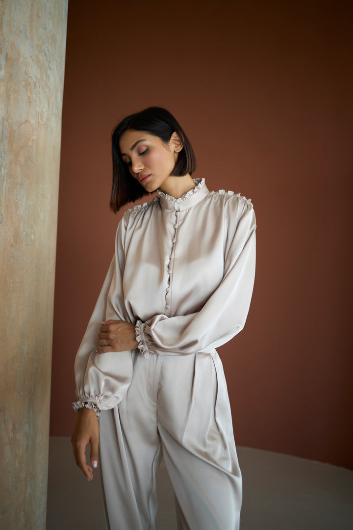 Woman wearing a light-colored blouse and pants against a warm-toned wall.