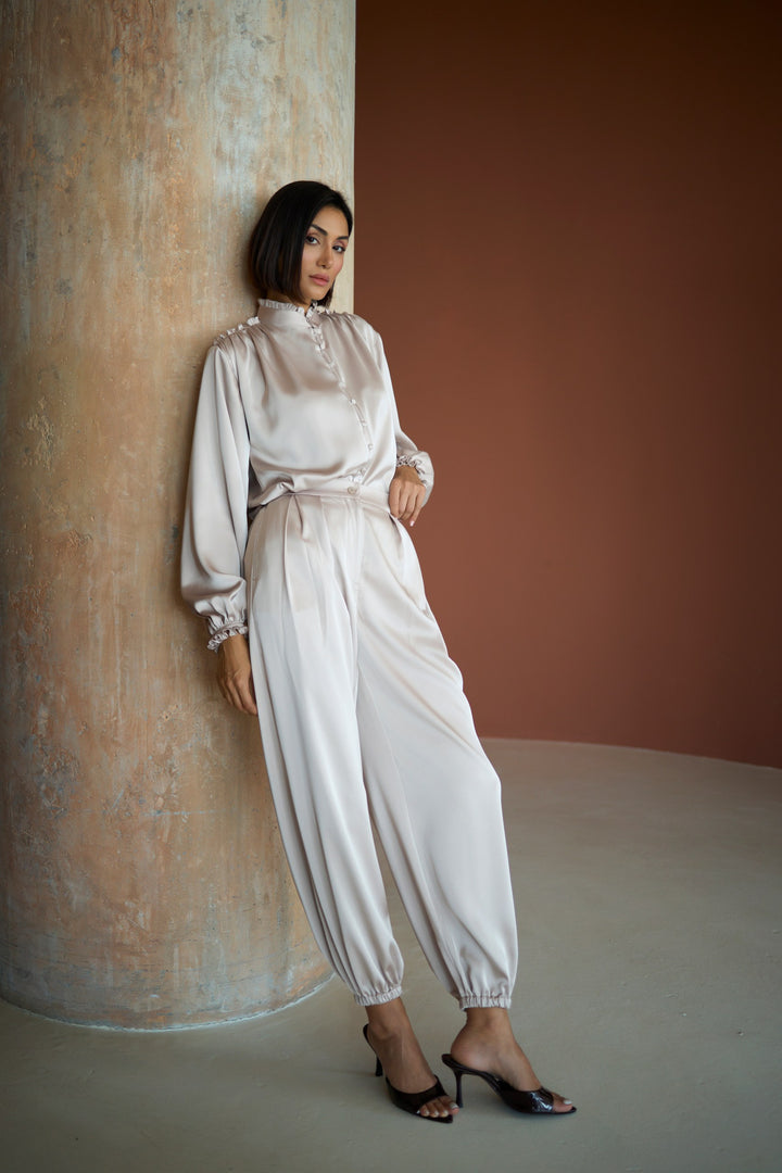 Woman in a white outfit leaning against a textured wall.