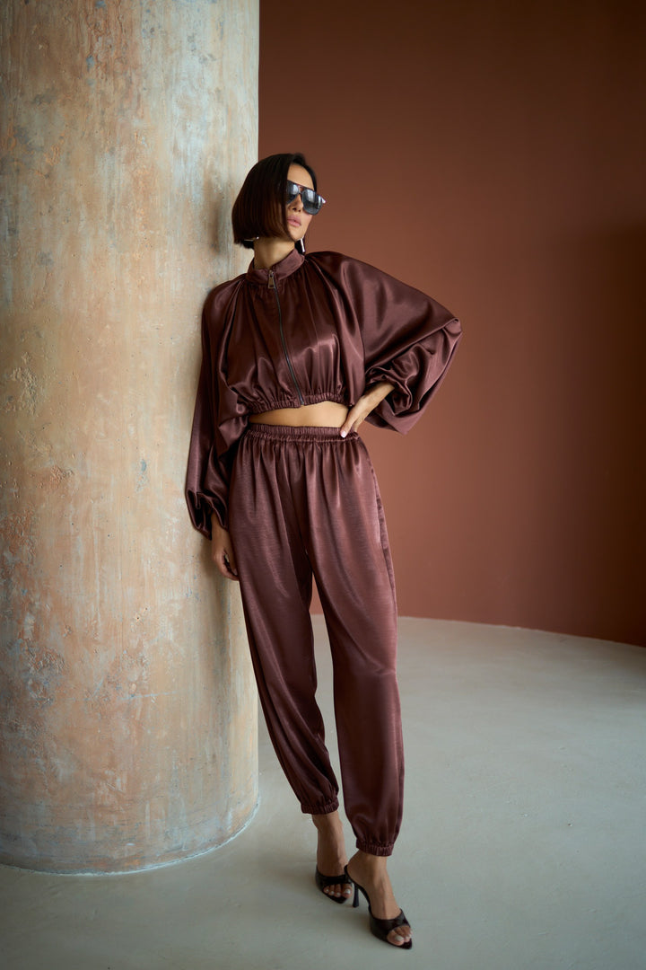 Woman in a brown satin outfit standing against a textured wall.