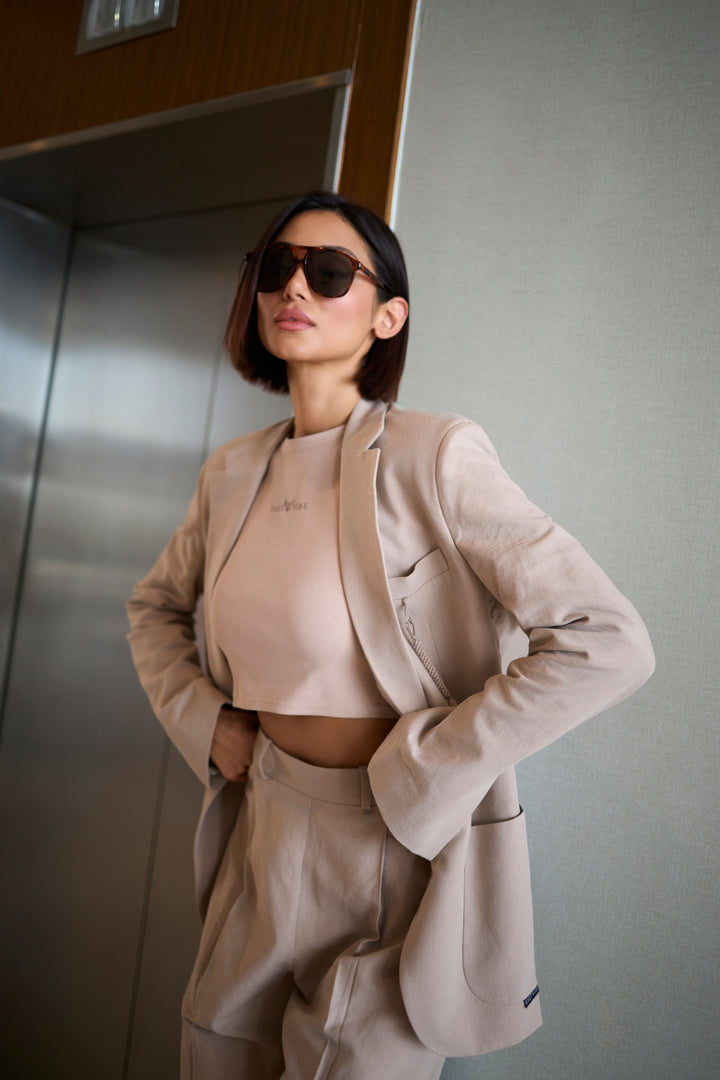 Woman in a beige suit standing against a neutral wall.