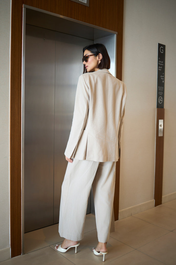 Woman in a beige suit standing in front of an elevator.
