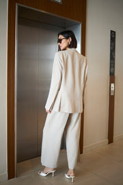 Woman in a beige suit standing in front of an elevator.