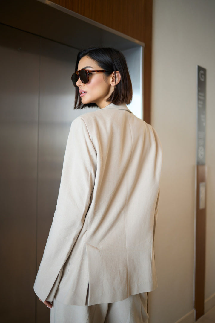 Woman wearing a beige outfit and sunglasses, standing in an elevator.